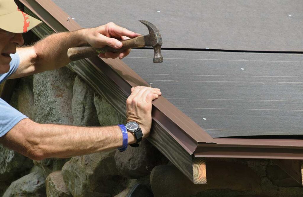 Homeowner examining worn shingles and ice buildup along a roof edge after winter weather.